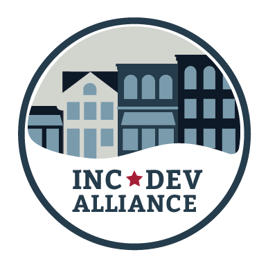 A circular logo featuring stylized city buildings in shades of blue, gray, and navy, with the text 'INC DEV ALLIANCE' and a small red star below, on a white background.